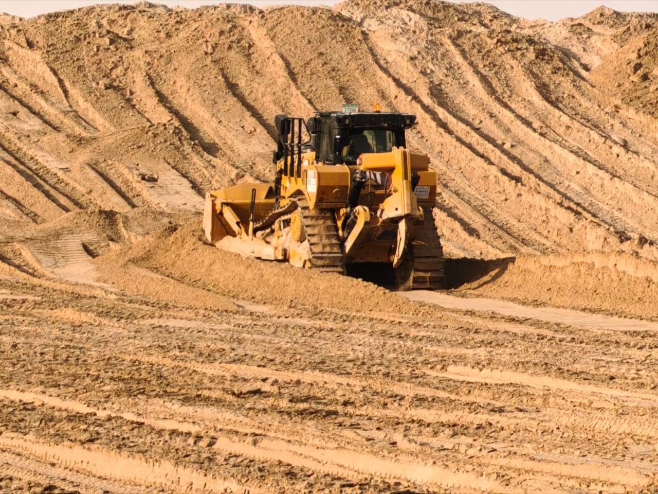 A yellow bulldozer moving earth on a sandy construction site