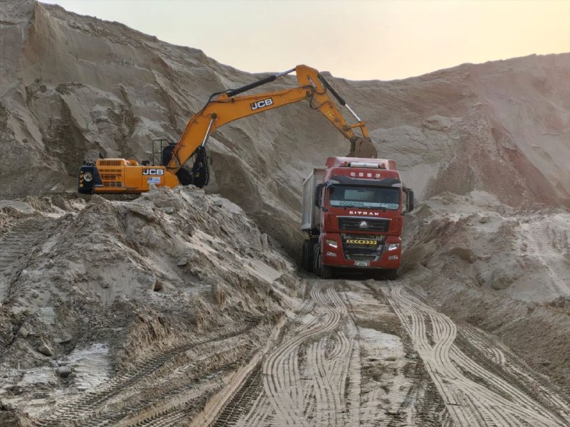 A yellow excavator loading a red dump truck at an earthworks site