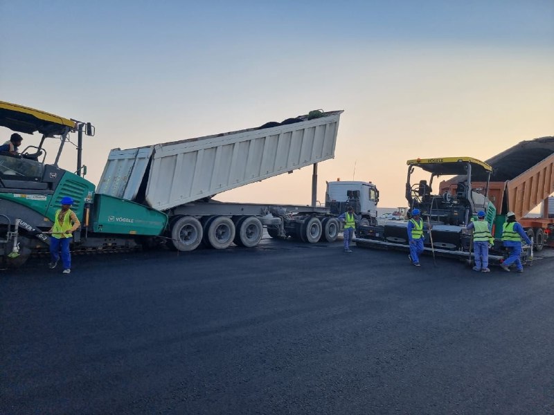 Road construction crew laying asphalt with paving machines and dump trucks